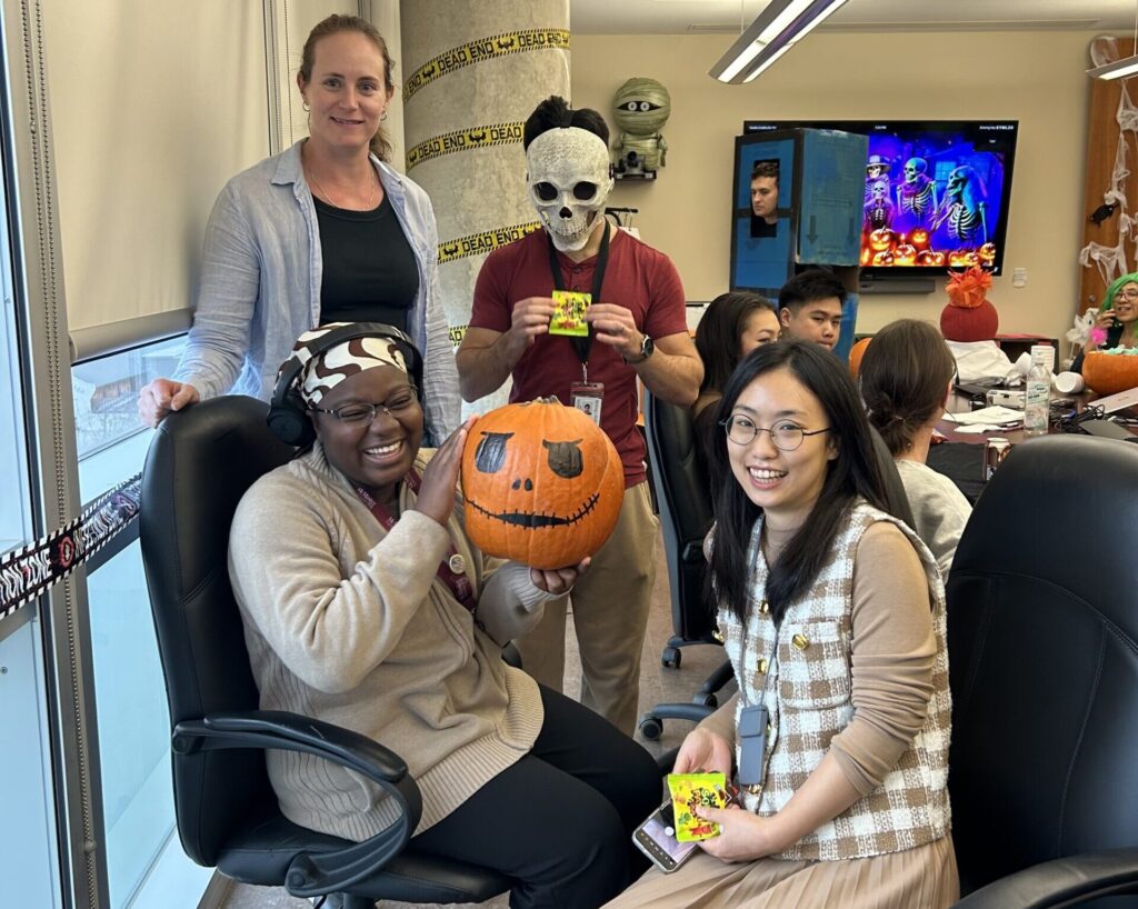 a group of people in an office hold a pumpkin and have halloween masks and candy